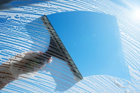 cleaning,soapy,windows,with,squeegee,against,sunny,blue,sky.,spring