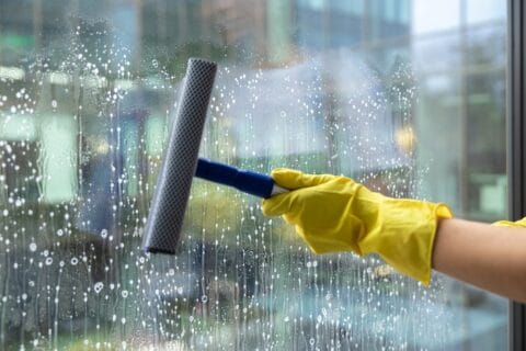 Woman in yellow gloves rubbing the window with the window washer
